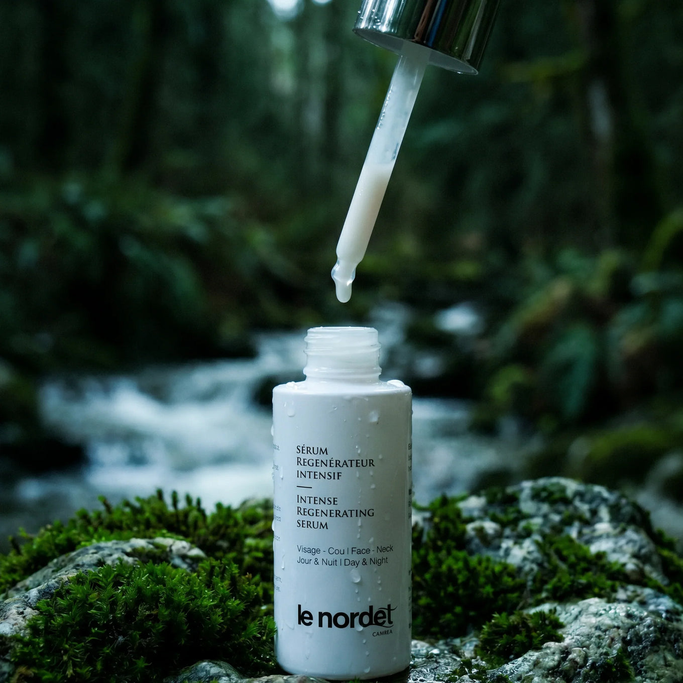 Intense regenerating serum bottle with dropper, set against a forest stream backdrop, highlighting natural skincare.