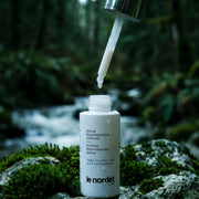 Intense regenerating serum bottle with dropper, set against a forest stream backdrop, highlighting natural skincare.